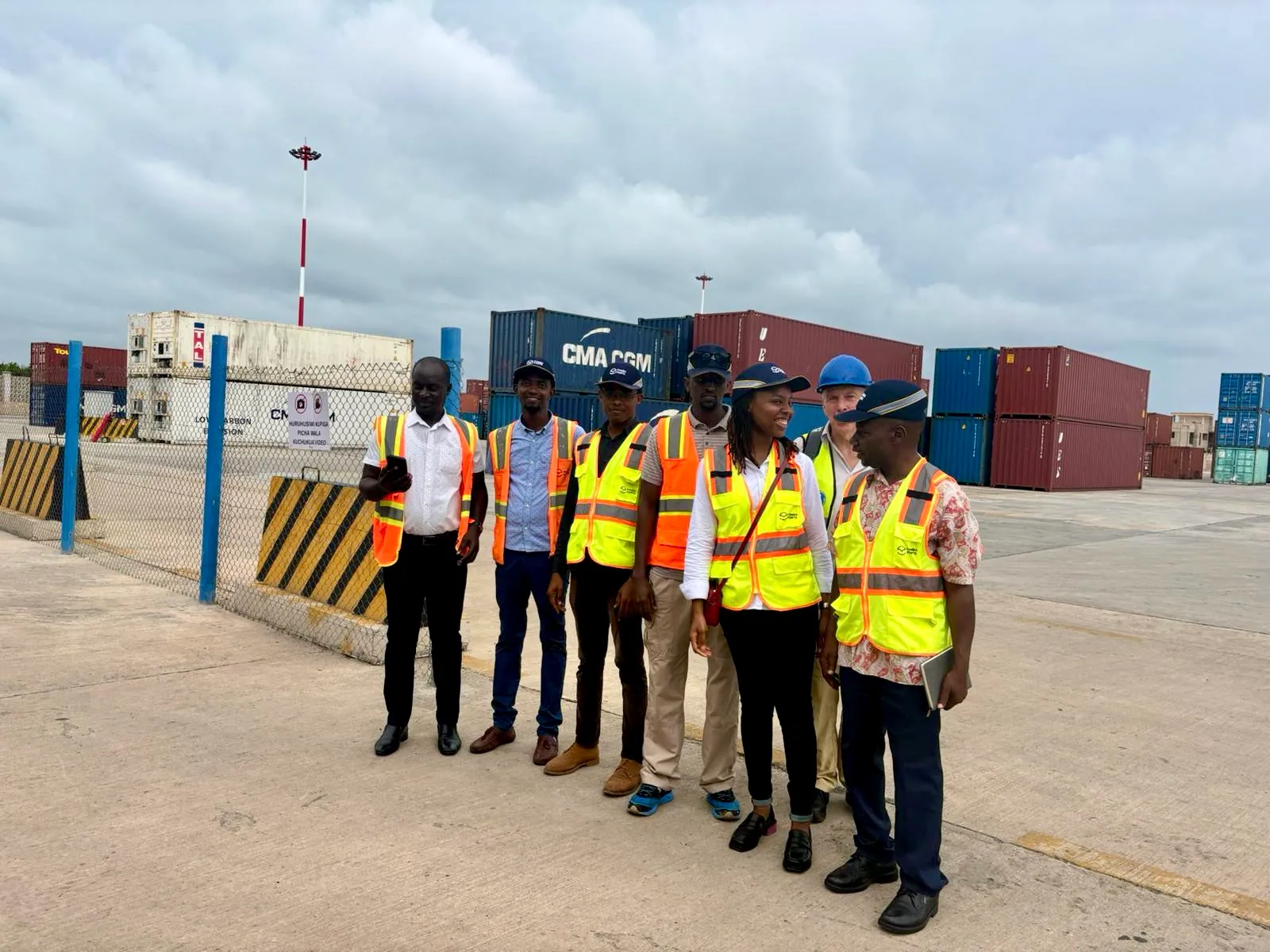 Émmage project team and port staff in high-visibility vests standing together on a container terminal apron, stacked shipping containers behind them